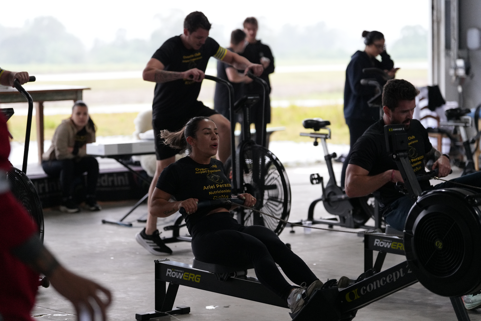 Participantes treinando em remo ergômetro e airbike no hangar do aeroporto durante a Airport Experience, transformando o local em arena de competição