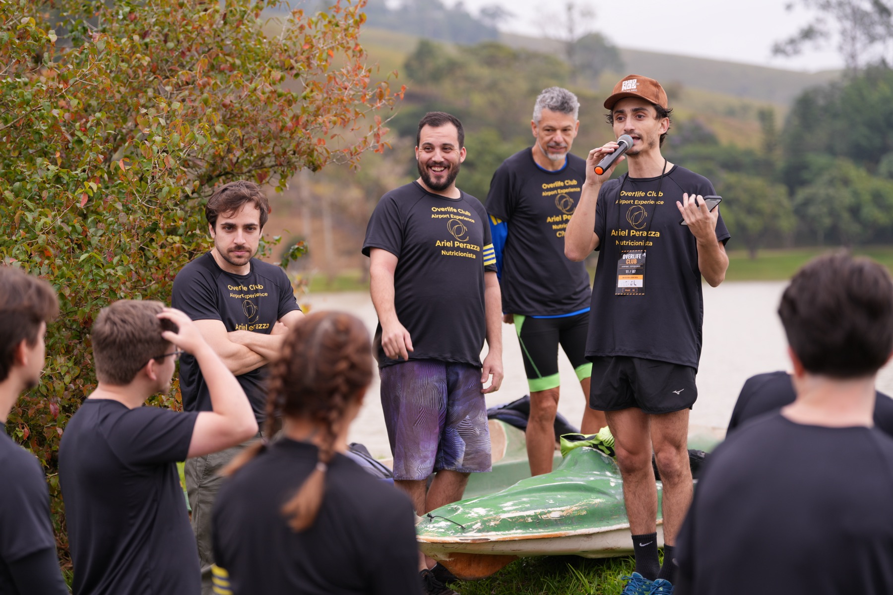 Ariel Perazza fala ao microfone com as equipes reunidas à beira do lago na Airport Experience