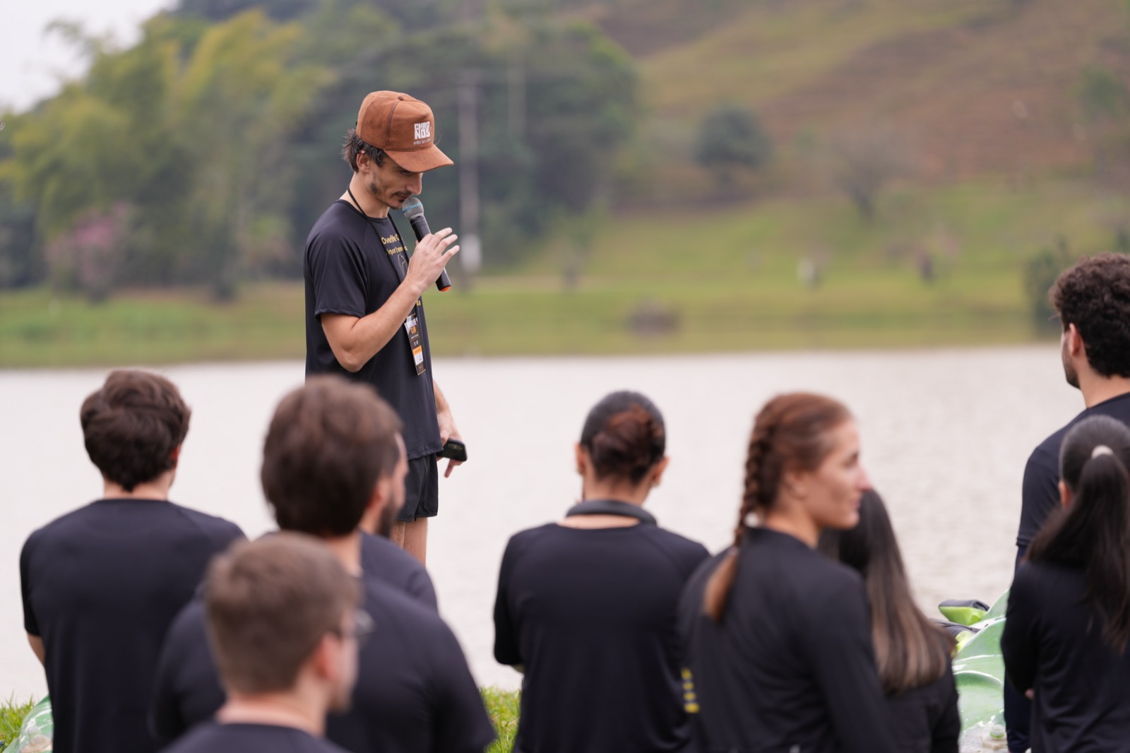 Ariel Perazza falando ao microfone para o grupo de participantes reunido à beira do lago durante a Airport Experience