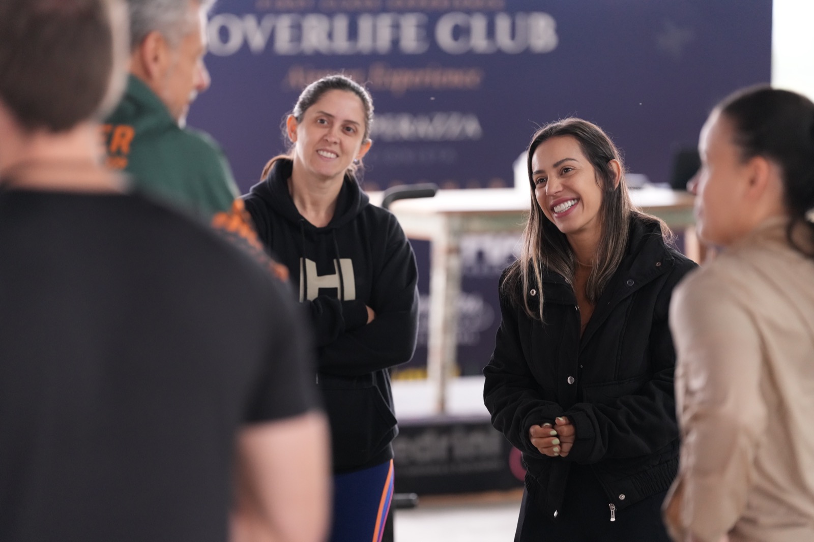Participantes sorrindo e conversando em frente ao painel Overlife Club Airport Experience