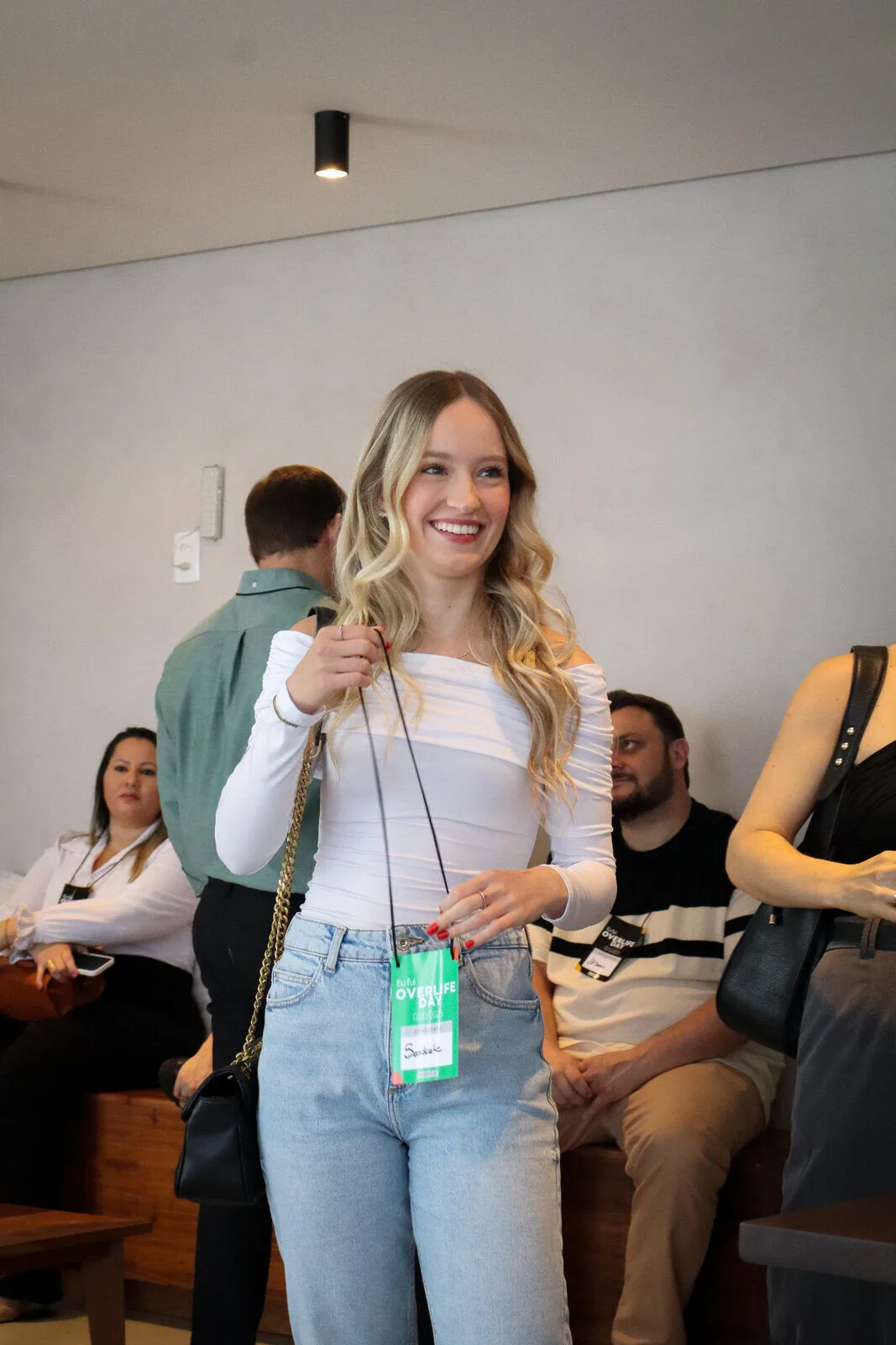 Convidada sorrindo com credencial do Overlife Day 2025 entre os participantes